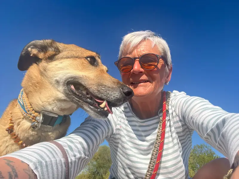 Katrin Bauer mit Sonnenbrille und einem Hund, der ihr ein Küsschen gibt